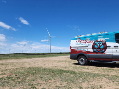 A picture of a Steadfast Heating & Air Work Vehicle in a field with wind turbines behind it.