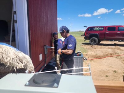 A picture of two guys installing an air conditioning unit outside of a building.