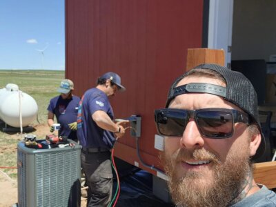 A picture of three guys installing an air conditioning unit to a building outside.