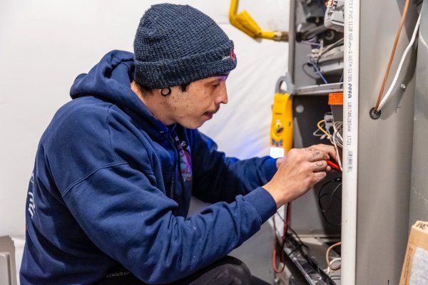A picture of a guy working on wires inside of an air conditioning unit.